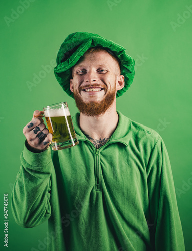 Lucky charms on green background. Portrait of excited man holding glass of beer on St Patrick's day isolated on green. Man on green background celebrate St Patricks Day. photo