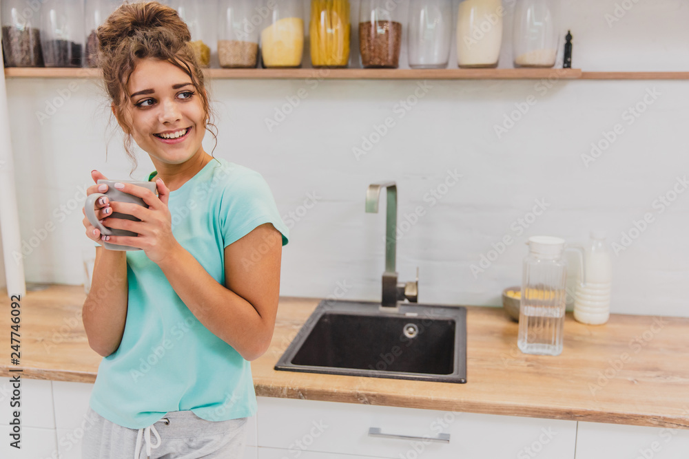 Gorgeous, beautiful, young woman holding glass of fresh water and smiling while standing in kitchen in the morning Gorgeous, beautiful, young woman holding glass of fresh water and smiling while standing in kitchen in the morning