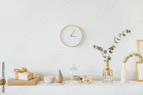 Modern interior design concept. Bright beige and golden apartment with clock, eucalyptus branch, vase, candle.