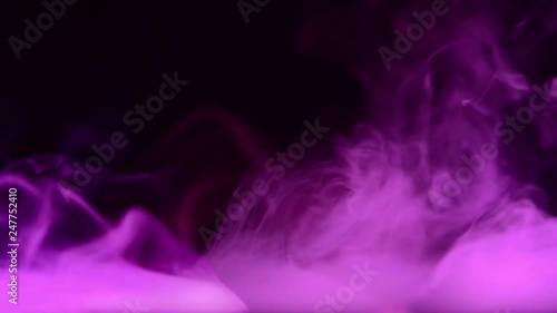 purple smoke waves over calm water surface at dark background