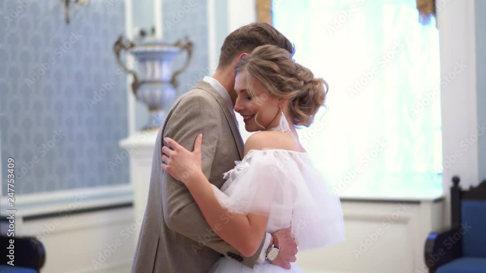 beautiful blonde bride in wedding dress is dancing with her fiance in a chic room beautiful blonde bride in wedding dress is dancing with her fiance in a chic room