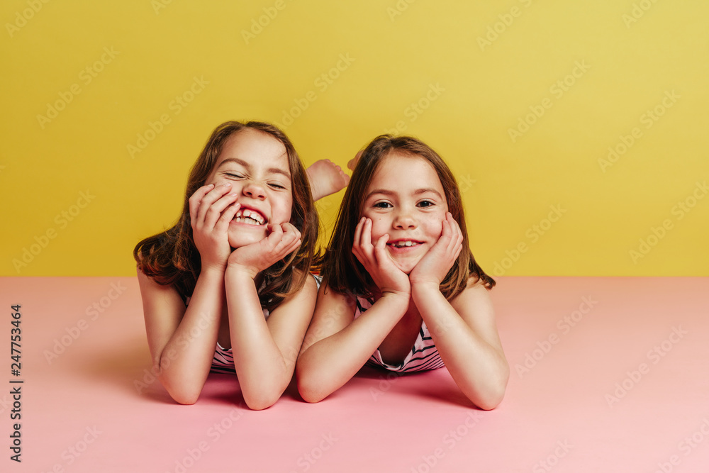 Twin girls lying on pink floor - obrazy, fototapety, plakaty 
