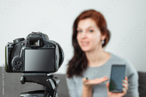 A young beautiful girl is sitting in front of a DSLR and recording a Vlog, close-up. Blogger, blogging, technology, online money, online courses. copy space.