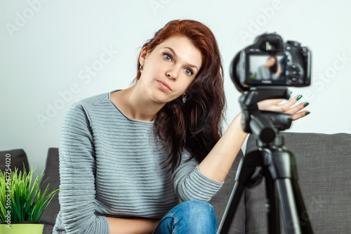 A young beautiful girl is sitting in front of a DSLR and recording a Vlog, close-up. Blogger, blogging, technology, online money, online courses. copy space.