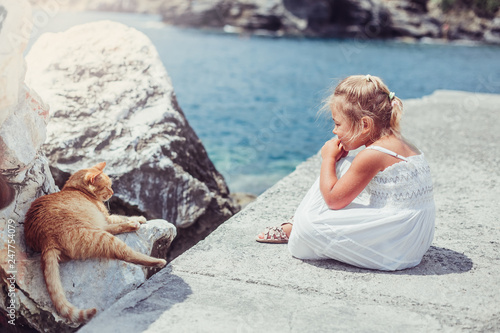 Little adorable cute girl sitting with cat on the coast of sea