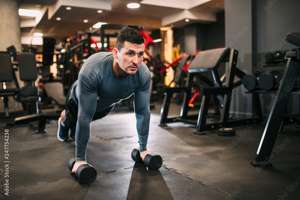 Confident muscular man in sportswear stand in plank position, on weights, during workout at the gym. Confident muscular man in sportswear stand in plank position, on weights, during workout at the gym.