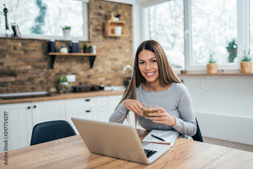 Beautiful young woman in the morning with laptop and coffee at the kitchen table.