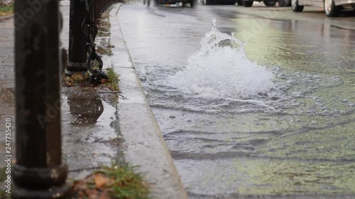 Footage of water comming out from a road drainage due to a ruptured water pipe under the ground, a car passing by...