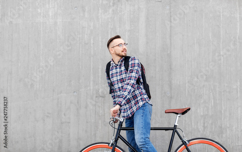 travel, tourism and lifestyle - happy young hipster man in earphones with fixed gear bike and backpack on city street