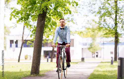 people, style and lifestyle - happy young hipster man riding fixed gear bike on city street