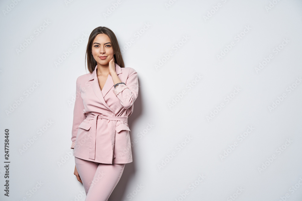 Woman wearing pink suit standing by white wall Woman wearing pink suit standing by white wall