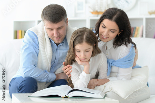 parents and daughter reading big book in room
