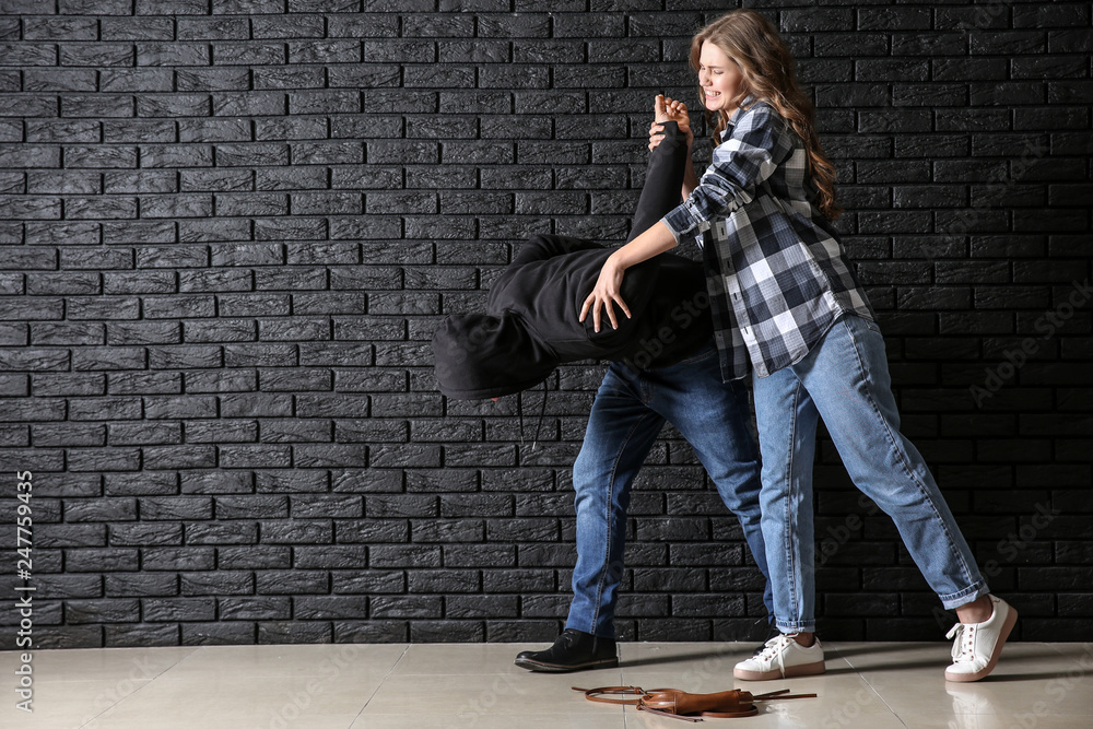 Young woman defending herself from attack by thief near dark brick wall - obrazy, fototapety, plakaty 