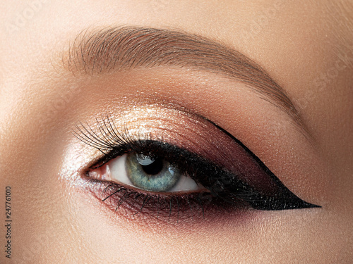 Close up of beautiful woman eye with multicolored fashion makeup and modern eyeliner wing. Studio shot photo