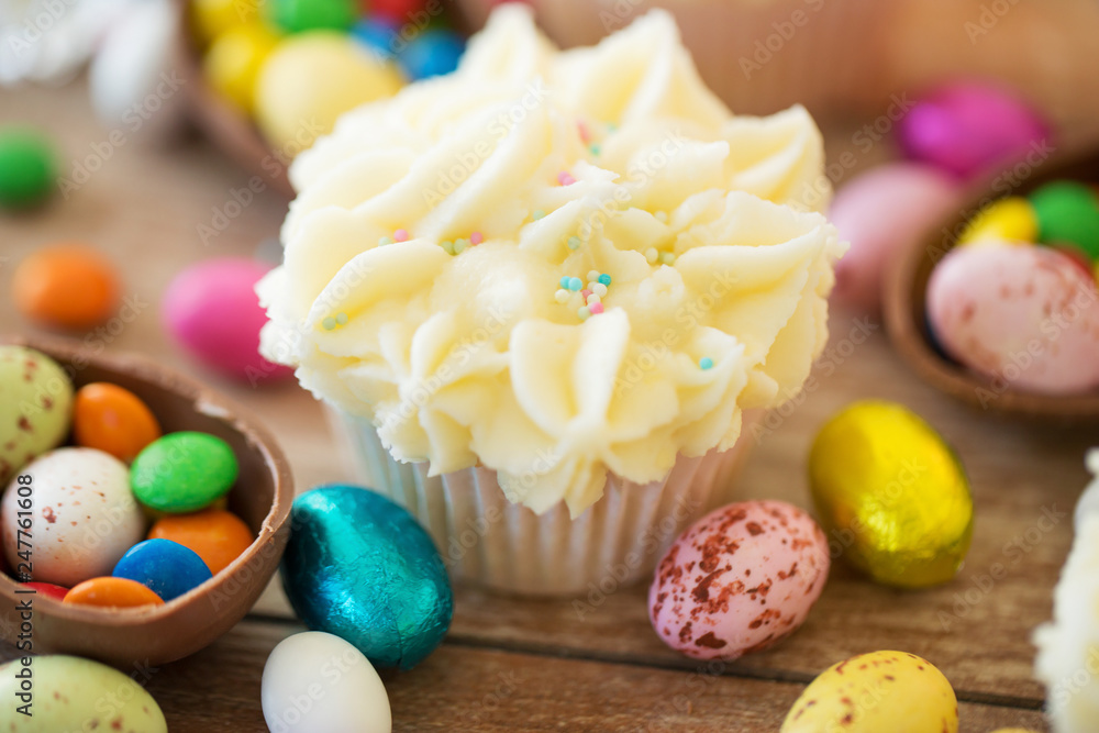 easter, food and sweets concept - frosted cupcakes with chocolate eggs and candies on table easter, food and sweets concept - frosted cupcakes with chocolate eggs and candies on table