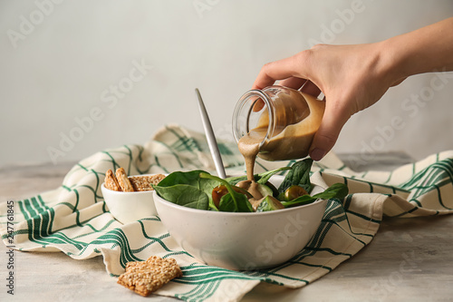 Pouring of tasty tahini from jar onto fresh vegetables in bowl photo