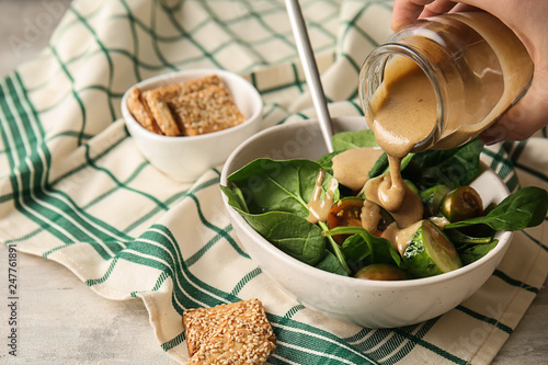 Pouring of tasty tahini from jar onto fresh vegetables in bowl photo