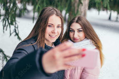 Two young cheerful girlfriends taking selfie in the winter outside - lifestyle