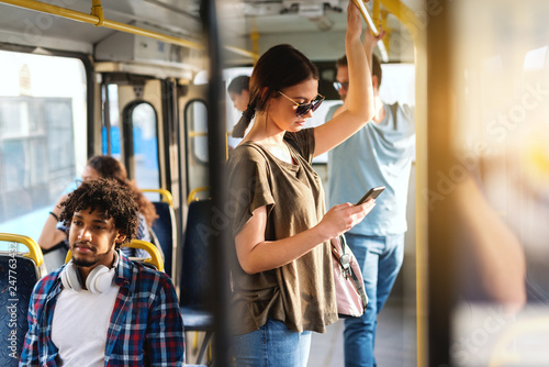 Caucasian girl driving in public bus and using smart phone for reading or writing message.
