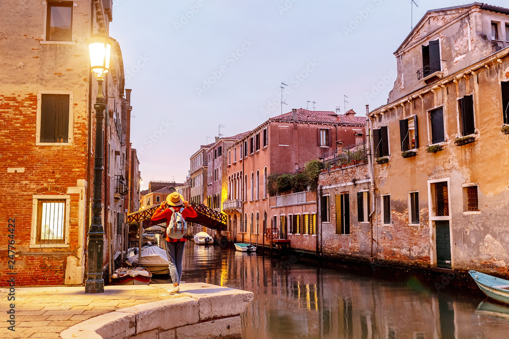 Young happy asian traveler woman on the pier of a narrow canal and street in Venice. Vacation in Italy concept