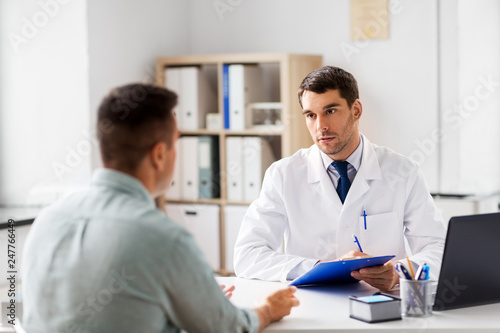 medicine, healthcare and people concept - doctor with clipboard talking to male patient at medical office in hospital