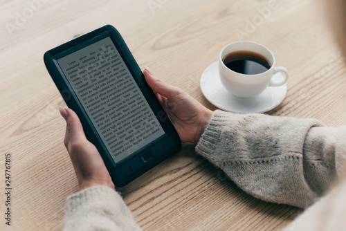 cropped view of woman studying with e-book near cup of coffee photo