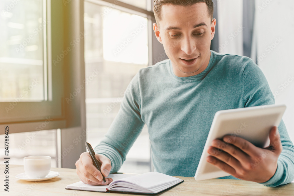 cheerful man studying with digital tablet while writing in notebook