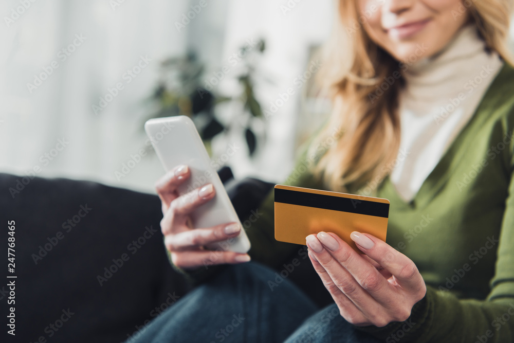 cropped view of woman holding smartphone and credit card in hands - obrazy, fototapety, plakaty 