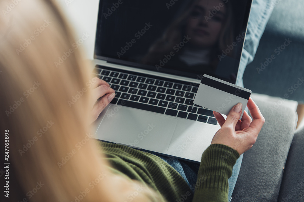 selective focus of woman using laptop with blank screen while holding credit card selective focus of woman using laptop with blank screen while holding credit card