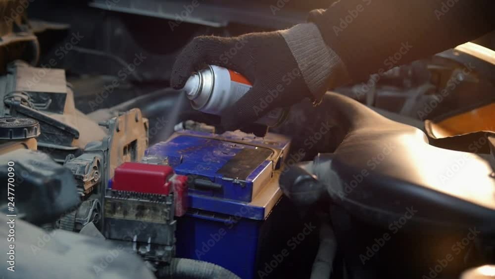 Car service. A mechanic man spraying paint on the battery Car service. A mechanic man spraying paint on the battery