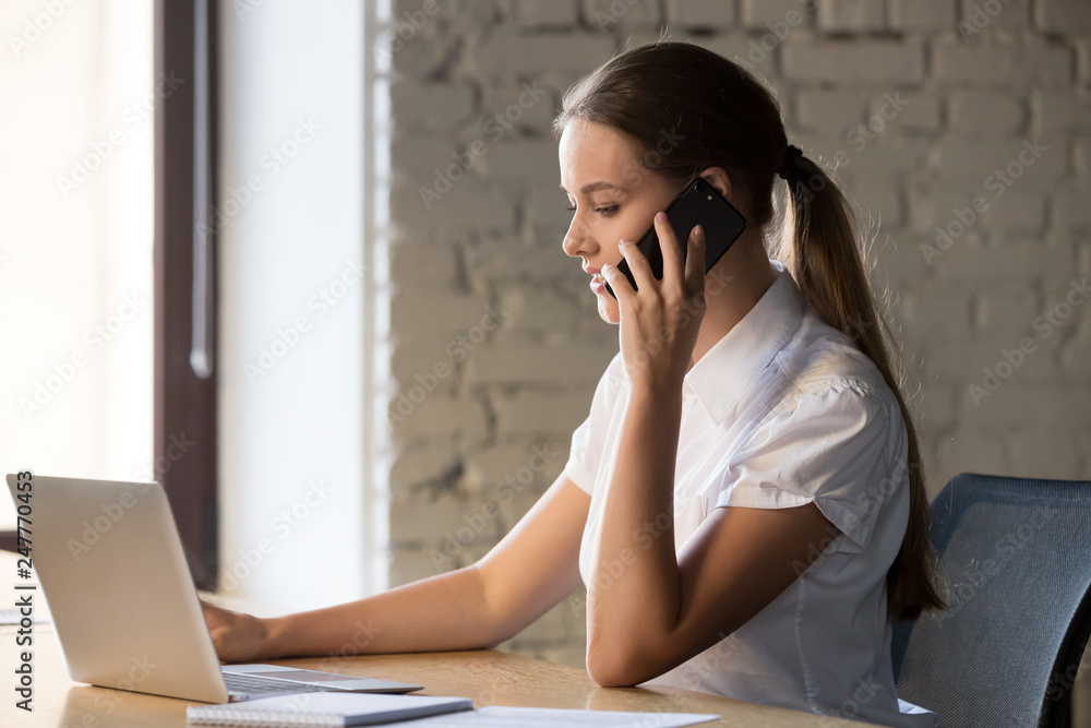 Focused female employee using laptop and talking on mobile Focused female employee using laptop and talking on mobile
