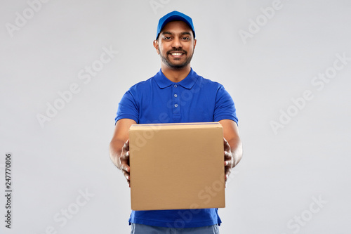 mail service and shipment concept - happy indian delivery man with parcel box in blue uniform over grey background photo