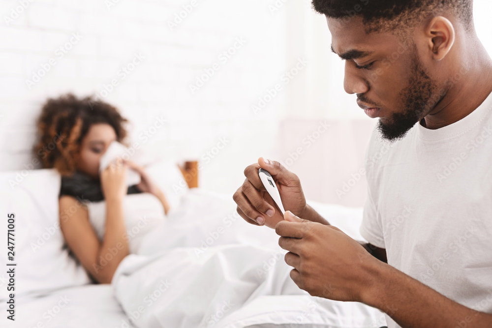 Sick woman in bed, man checking temperature on thermometer Sick woman in bed, man checking temperature on thermometer