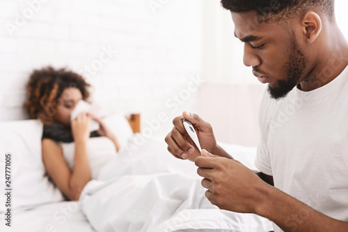 Sick woman in bed, man checking temperature on thermometer
