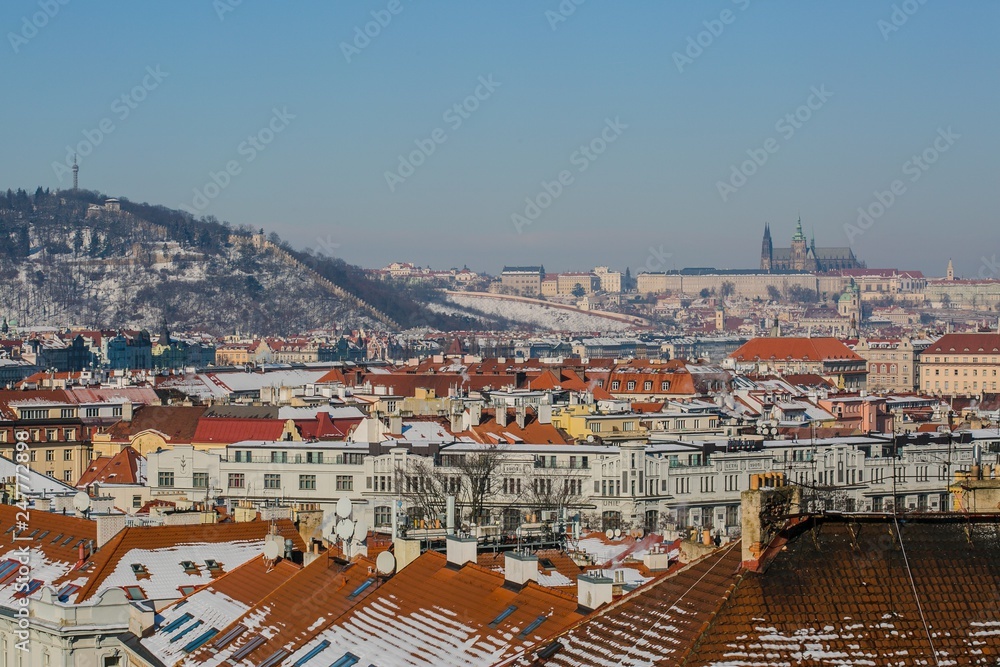 Prague, Czech Republic / Europe - February 5 2019: Scenic view of Prague city, Prague castle and Petrin tower from Vysehrad overlooking red roofs covered with snow, sunny day, clear blue sky