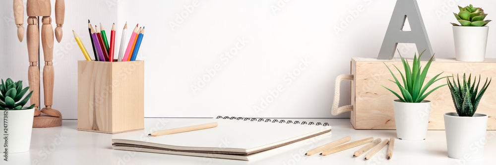 Creative hipster desk by the white wall with wooden accessories. Natural drawing space. Succulents, colored pencils, sketchbook and wooden figure of a man. Panoramic copy space for text - obrazy, fototapety, plakaty 