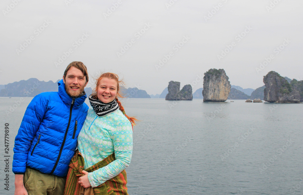 Young couple guy and girl in sportswear hugging and laughing happily against the background of the cliffs of Ha Long Bay during the honeymoon in Vietnam