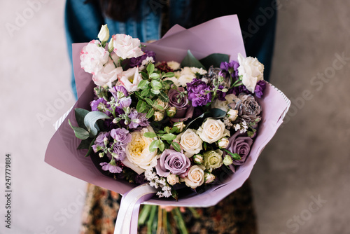 Wallpaper Mural Very nice young woman holding beautiful blossoming bouquet of fresh roses, mattiola, eustoma flowers in purple color on the grey wall background  Torontodigital.ca