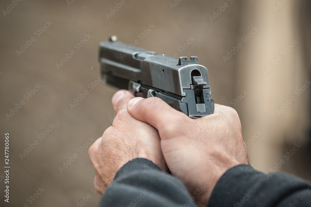 Shooter holding gun in hand and shooting. Close-up detail view Shooter holding gun in hand and shooting. Close-up detail view