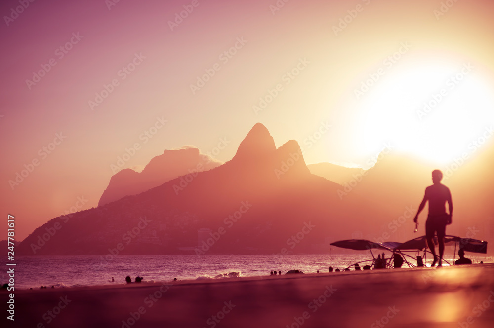 Scenic golden sunset view of Ipanema Beach with shadow silhouettes walking on the Arpoador boardwalk in Rio de Janeiro, Brazil