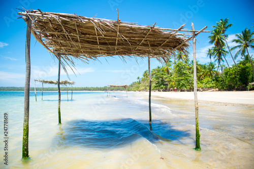 Rustic palm frond and tree branch palapa umbrella waiting to shade visitors to the shallow waters on a remote palm fringed tropical beach in Bahia, Brazil photo