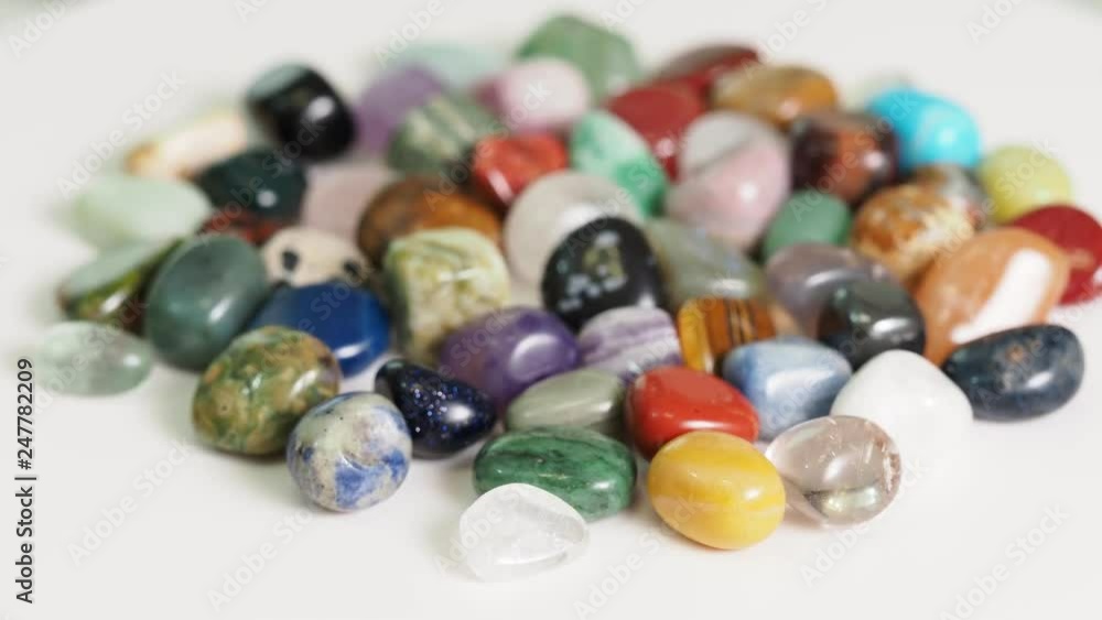 handful of various tumbled gemstones rotating on white table handful of various tumbled gemstones rotating on white table