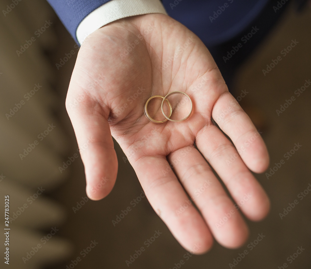 Close up top view of opened palm of man holding two golden wedding rings. Groom or groomsmen ready for wedding ceremony. Color photography.