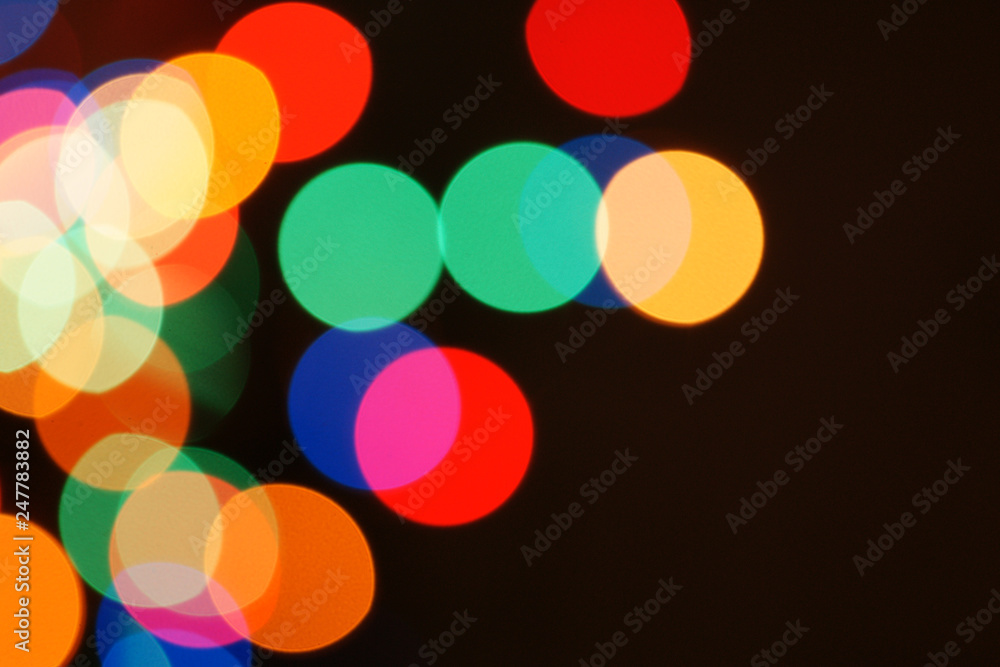 Multi-color holiday garland. Garland is blurred. Many colorful round lights. Fully defocused photo. Blurred background and foreground. Holiday mood. New Year and Christmas is coming.