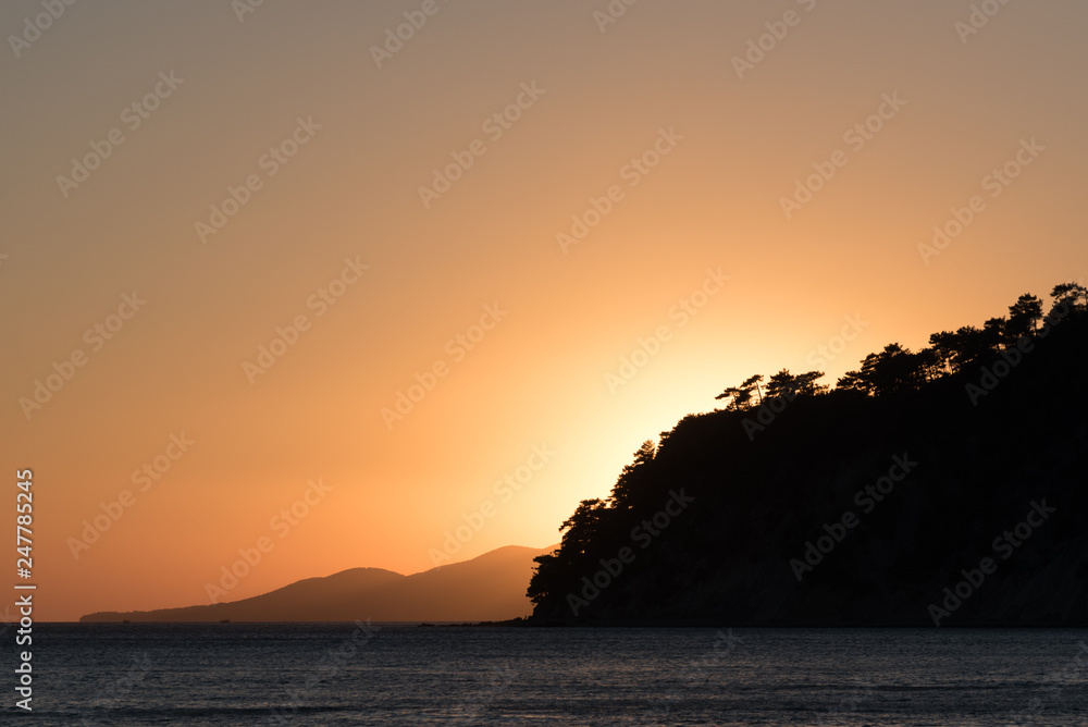 Sunset on sea. Silhouette of the mountain overgrown with trees at sunset.