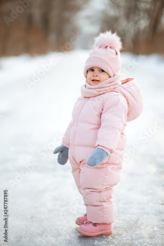 Little beautiful girl in pink jumpsuit in a snowy winter park