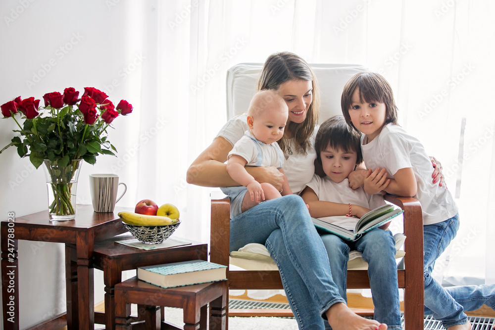 Mother, playing with her toddler boy and his older brother, reading book, smiling Mother, playing with her toddler boy and his older brother, reading book, smiling