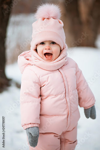 A beautiful young girl wearing a pink jumpsuit running in a snowy winter park.
