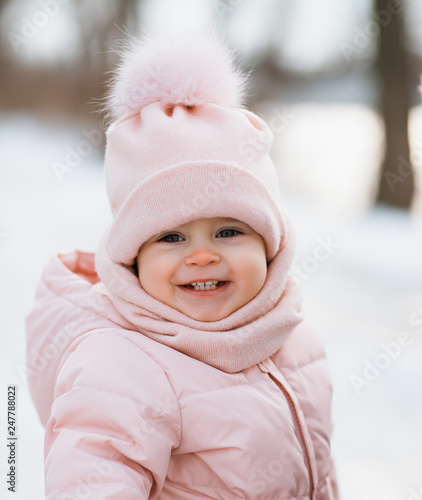 A beautiful young girl wearing a pink jumpsuit running in a snowy winter park.