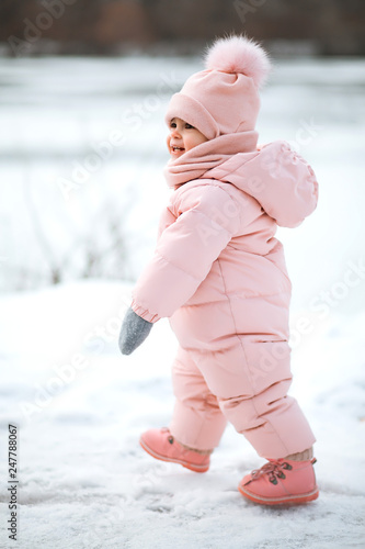 A beautiful young girl wearing a pink jumpsuit running in a snowy winter park.